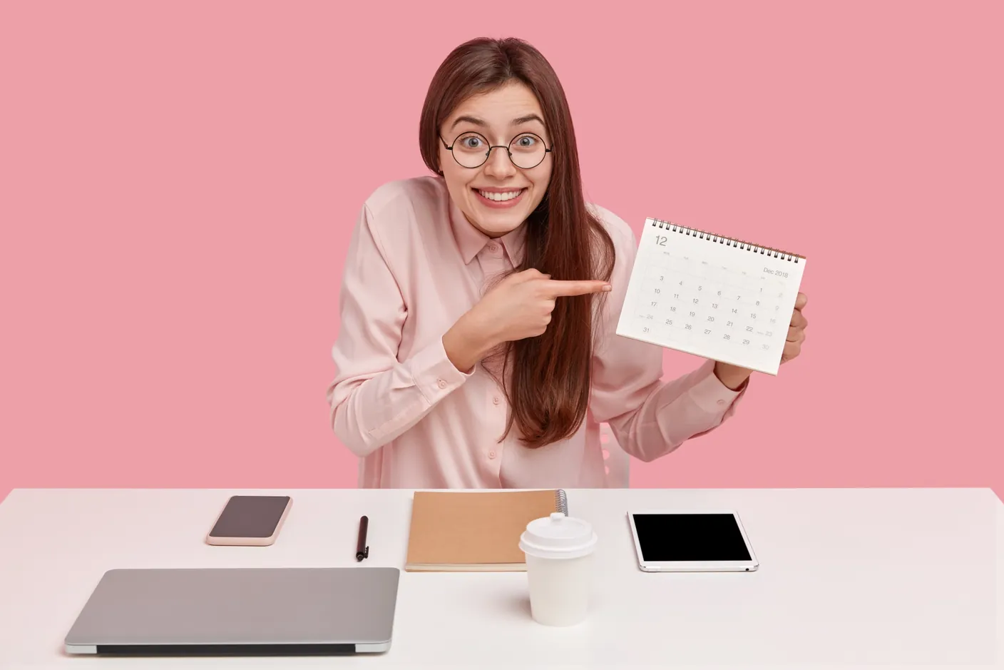 Mujer sonriente señalando un calendario en su escritorio para planear sus días de vacaciones.