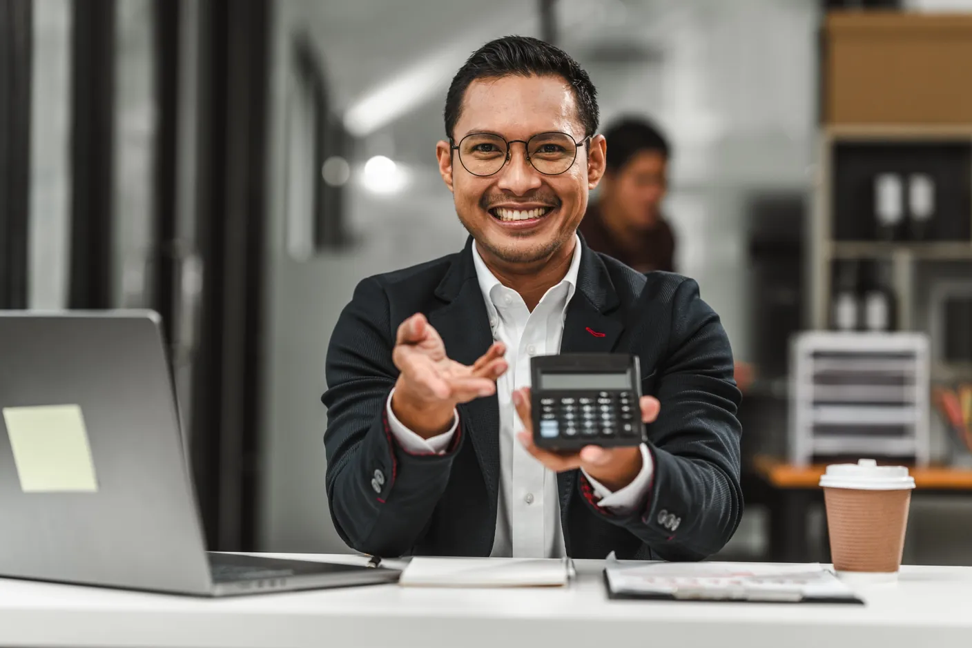 Hombre sonriente en su escritorio mostrando una calculadora para calcular el aguinaldo.